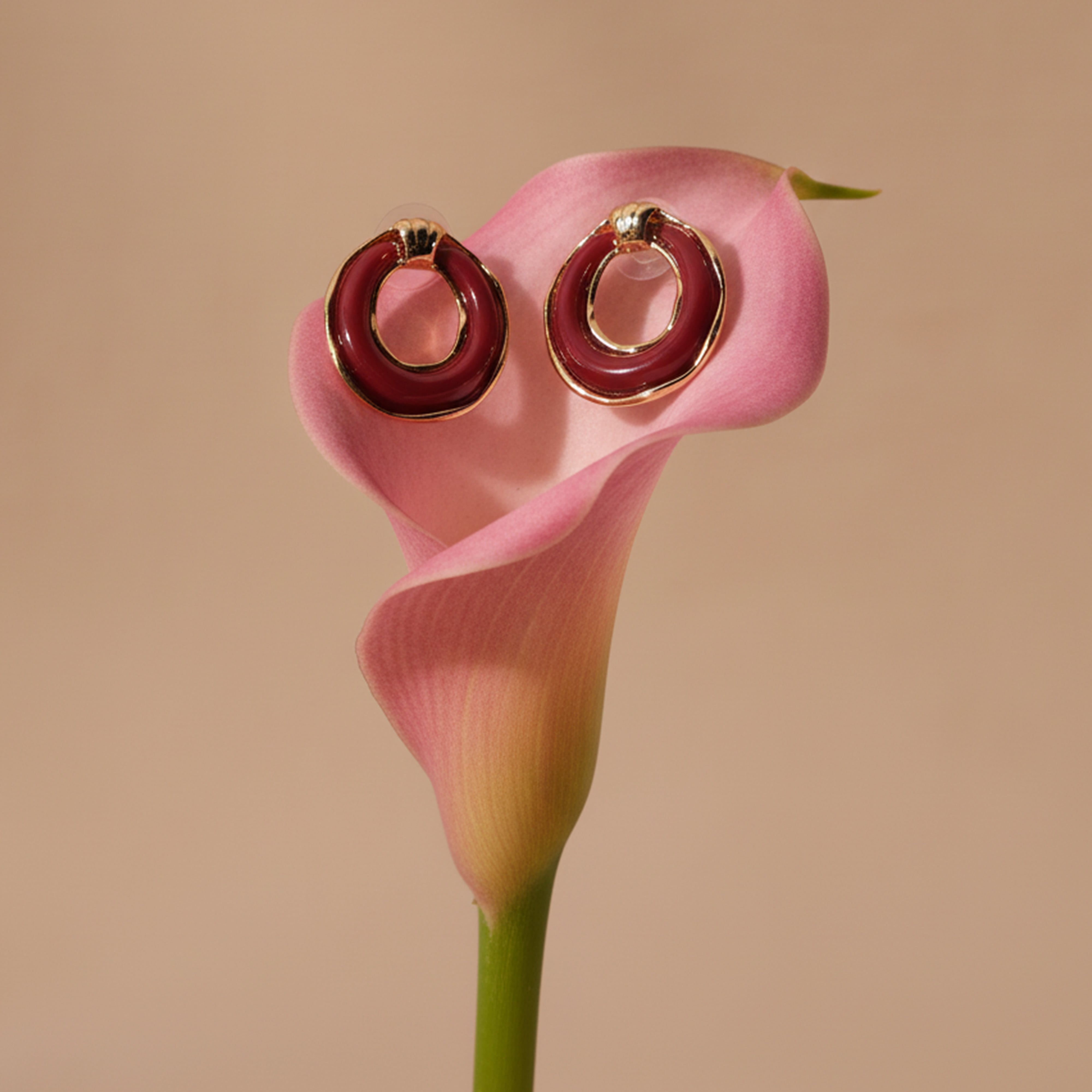 Red hoop earrings on a pink calla lily against a beige background